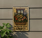 A metal sign with a floral design hangs on a wall, displaying the text "WINDOW BOX GARDEN".