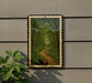a framed painting of a forest path, with a person walking along the path.