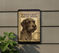 a sign with a dog illustration, mounted on a wall next to a plant.