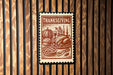 A Thanksgiving-themed stamp or postcard is displayed on a wooden wall, featuring illustrations of a turkey, pumpkin, pie, and candles.