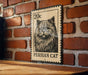 A metal sign featuring a Persian cat illustration is mounted on a brick wall.