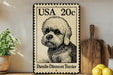 A vintage-style metal sign featuring a dandie dinmont terrier, with a postage stamp-like design, is displayed on a wooden shelf next to a potted plant and a wooden cutting board.