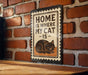 A metal sign with the text "HOME IS WHERE MY CAT IS" and an illustration of a cat is mounted on a brick wall.