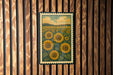A framed print of a field of sunflowers is displayed on a wooden wall.