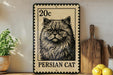 A metal sign featuring a close-up of a Persian cat, with a 20 cent stamp value, is displayed on a wooden shelf next to a potted plant and a wooden cutting board.