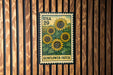 A vintage-style postage stamp featuring a field of sunflowers, mounted on a wooden wall.