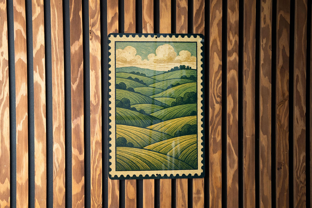 a framed painting of a countryside landscape, hanging on a wooden wall.