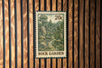 A 20c postage stamp with a landscape illustration is displayed on a wooden wall.