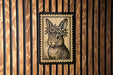 A framed illustration of a rabbit wearing a flower crown is displayed on a wooden wall.