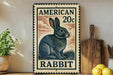 A vintage-style metal sign featuring an illustration of a rabbit, with the text "AMERICAN 20c RABBIT" printed on it. The sign is displayed on a shelf next to a wooden cutting board and some kitchen utensils.
