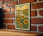 A framed image of a field of sunflowers is displayed on a brick wall.