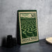 A metal sign with a green border and a maze illustration, featuring the text "HEDGE MZE" on it, is placed on a table next to some black camera lenses.