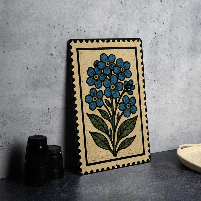 A framed artwork depicting a blue flower is displayed on a table, accompanied by a stack of black camera lenses and a white dish.