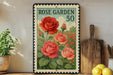 A framed vintage postage stamp featuring a vibrant illustration of red roses, placed on a wooden shelf next to a wooden cutting board and a potted plant.