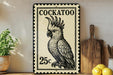 A vintage-style metal sign with a black and white illustration of a cockatoo, featuring the text "COCKATOO" and the price "25c". The sign is displayed on a shelf next to a wooden cutting board and a potted plant.