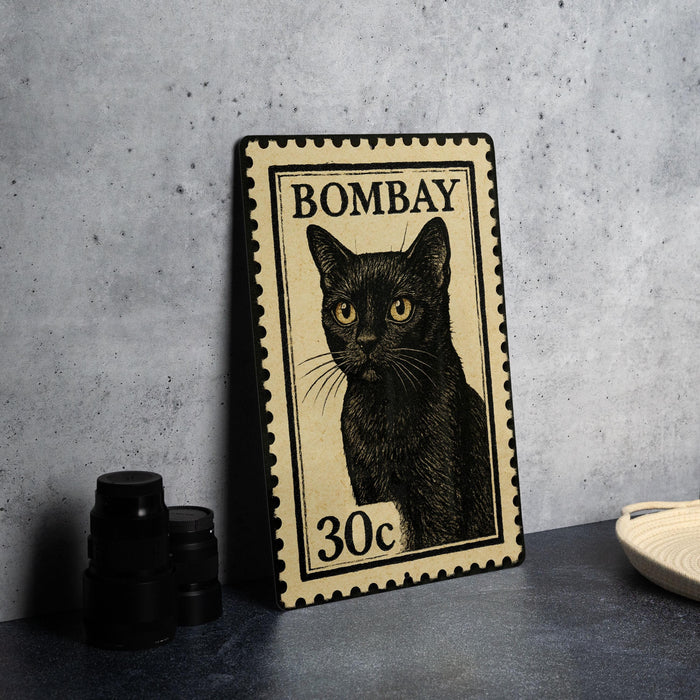 A framed stamp depicting a black cat, with the text "BOMBAY" and "30c" printed on it, is displayed on a table next to some black camera lenses.