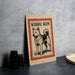 A sign featuring a dog illustration with the text "KISCHU KEN" on it, placed on a table next to some black camera lenses.