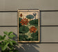 A framed painting of lotus flowers is displayed on a wall, with a plant visible to the left.