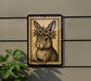 A decorative sign featuring a rabbit wearing a flower crown, mounted on a wall next to a plant.