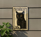 A black cat with yellow eyes is depicted on a stamp-like sign, mounted on a wall.