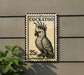 A postage stamp featuring a cockatoo, with the text "COCKATOO" and the value "25c" printed on it.