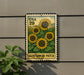 A metal sign with a sunflower design is mounted on a wall, with a plant visible to the left.