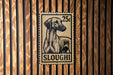 A 25c postage stamp featuring a dog's head is affixed to a wooden wall.