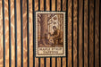 A wooden wall with a framed illustration depicting a person tapping a tree to collect maple syrup.