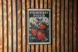 A vintage-style postage stamp featuring a strawberry patch, mounted on a wooden wall.