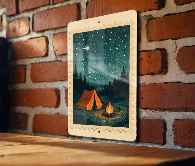 A framed illustration of a camping scene with a tent, campfire, and starry night sky is displayed on a brick wall.