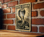 A black and white illustration of a cobra on a 20 cent stamp is displayed on a brick wall.