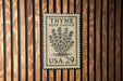 A vintage-style postage stamp with the text "THYME HERB GARDEN USA.29" is displayed on a wooden wall.