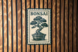 A metal sign with the word "BONSAI" and an illustration of a bonsai tree is mounted on a wooden wall.