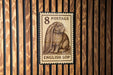 A brown rabbit on a brown postage stamp with the text "8 POSTAGE ENGLISH LOP" is displayed against a wooden background.