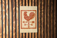 a sign with a rooster and a weather vane, mounted on a wooden wall.