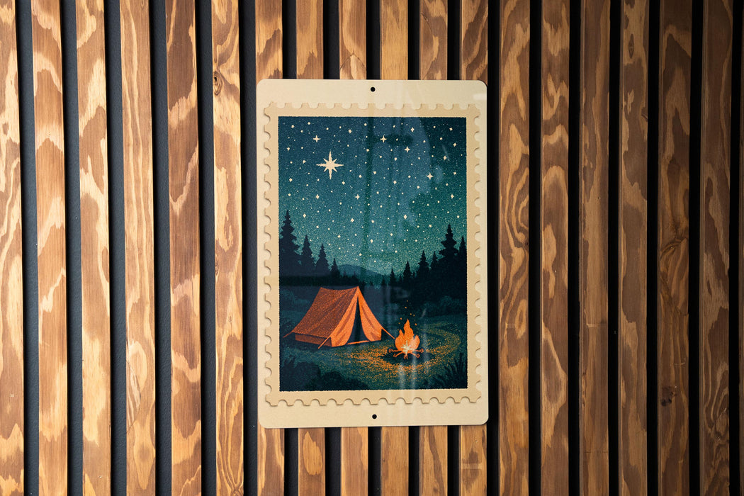 A framed image of a tent set up in a forest, with a campfire nearby, is displayed on a wooden wall.