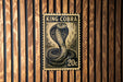 A black and white stamp-like image of a king cobra is displayed on a wooden wall.