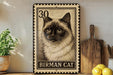 A framed image of a Siamese cat, with the text "BIRMAN CAT" printed on it, is displayed on a shelf next to a wooden cutting board and some kitchen utensils.