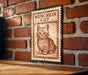 A metal sign with a cat illustration on it, mounted on a brick wall.