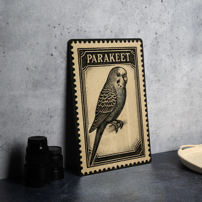 A framed illustration of a parakeet, a small parrot, is displayed on a table next to some black camera lenses.