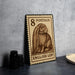 A wooden postcard with an illustration of an English lop rabbit on it, placed on a table next to some black camera lenses.