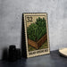 A metal stamp with a garden bed illustration on it, placed on a countertop next to some black camera lenses.