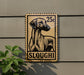 A 25c postage stamp featuring a dog on a brown background, mounted on a wall next to a plant.