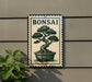 a sign with a bonsai tree illustration, mounted on a wall next to a plant.