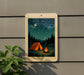A framed image depicting a camping scene with a tent, campfire, and starry night sky.