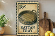 A 15 cent stamp-like sign with a drawing of a woven basket, placed on a wooden surface next to a wooden cutting board and some lemons.