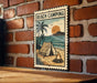 A vintage-style metal sign with a beach camping scene, featuring a tent, palm trees, and a campfire on a sandy beach.