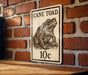 A sign featuring a toad illustration and the text "CANE TOAD 10c" is displayed on a brick wall.