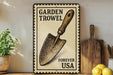 A vintage-style metal sign with a shovel illustration, placed on a wooden shelf next to a potted plant and kitchen utensils.