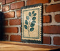 a wooden table with a framed print of a leafy plant on the wall behind it.